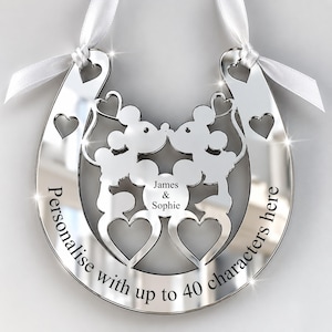 May include: A silver-toned horseshoe ornament featuring two mouse silhouettes kissing, heart cutouts, and white ribbon ties. The text "James & Sophie" is engraved in the centre, with "Personalise with up to 40 characters here" along the bottom edge.