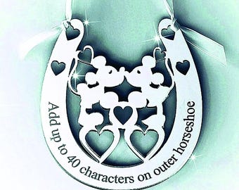 May include: Silver horseshoe ornament with Mickey and Minnie Mouse silhouettes kissing, surrounded by hearts. Text reads "Add up to 40 characters on outer horseshoe". White ribbon for hanging.