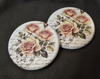 May include: Two round ceramic coasters featuring a cream-colored background with a vintage-style print of soft pink roses, green leaves, and black clock face illustrations overlaid with cursive script text that reads Loving you.