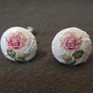 Peut inclure: Deux boutons de manchette ronds et blancs avec un motif de rose rose et des feuilles vertes. Les boutons de manchette ont une tige argentée. Chaque bouton mesure environ 2 cm de diamètre.