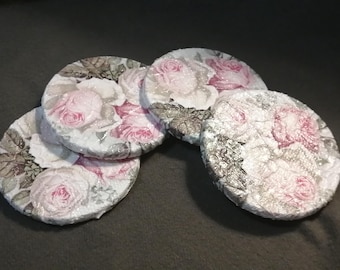 May include: A set of four circular coasters featuring a decoupage design of pink roses and green leaves on a white background. The surface of each coaster has a textured, glossy finish with visible crinkled paper patterns throughout.
