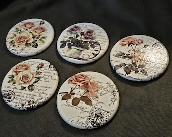 May include: A set of five round ceramic coasters featuring floral designs with pink roses, green leaves, and black cursive script text. Each coaster displays a unique arrangement of botanical illustrations, vintage-style stamps, and clock motifs.