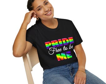 Op de afbeelding: Zwart t-shirt met het woord "PRIDE" in regenboogkleuren en de tekst "Free to be ME" in het wit. Het shirt is gemaakt van een zacht materiaal.