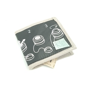 Puede incluir: Una cartera negra con un diseño blanco de un altavoz e instrucciones sobre cómo doblarla. La cartera tiene un borde beige y una pequeña etiqueta verde con el texto "KIK" en ella.