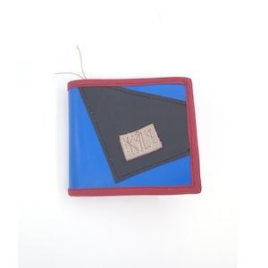 Puede incluir: Una cartera de cuero azul y negro con un borde rojo y una pequeña etiqueta de color beige que dice "KIKA".