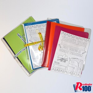 May include: A collection of colorful folders and cards with the text "THANK YOU FOR BEING A GREAT TEACHER". The folders are in various colors, including green, blue, orange, and pink. A yellow measuring tape is wrapped around some of the folders.