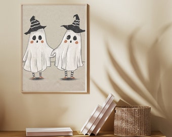 May include: A framed wall art print featuring two white ghosts wearing black witch hats with white stripes, black and white striped leggings, and orange shoes. The ghosts have round black eyes, small mouths, and pink cheeks, standing on a light tan background.
