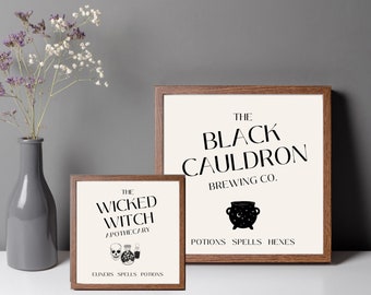 May include: Two square wooden frames containing white prints with black text. The smaller print reads THE WICKED WITCH APOTHECARY with skull and bottle icons. The larger print reads THE BLACK CAULDRON BREWING CO. with a cauldron icon.