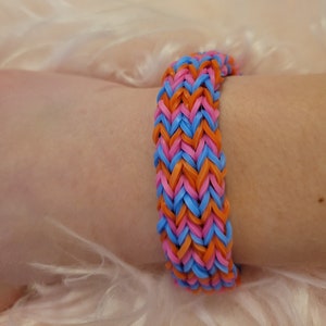 May include: A colorful rubber band bracelet with a chevron pattern in pink, blue, and orange.
