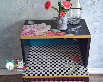 May include: A decorative black side table with a floral and dragonfly design on the top. The drawer features pink and white stripes and a decorative knob. A vase of pink flowers and a glass bottle are on top.