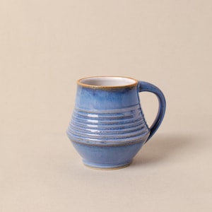 May include: A blue ceramic mug with a white interior and a brown rim. The mug has a rounded body with a textured, striped design.