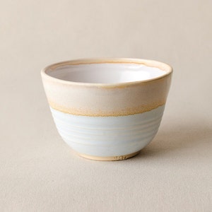 May include: A small, white ceramic bowl with a light blue glaze and a band of brown glaze around the top.