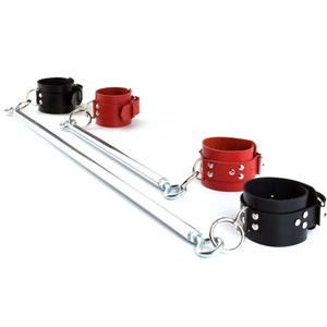 May include: A spreader bar featuring two parallel silver-toned metal rods connected by swivel eye bolts. Attached to the ends are four adjustable leather cuffs, two in black and two in red, each secured with silver-toned metal buckles and rivets.
