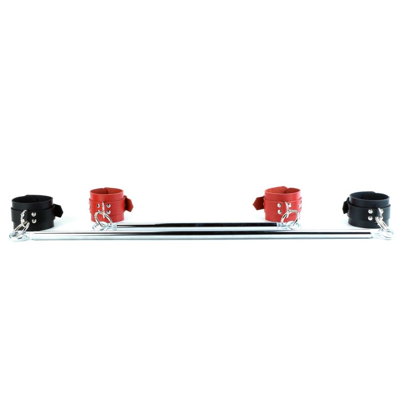 May include: A metal spreader bar featuring two black cuffs on the outer ends and two red cuffs positioned toward the center. Each cuff is secured with silver-toned metal rivets and attached to the bar using silver-toned metal rings and swivel clips.