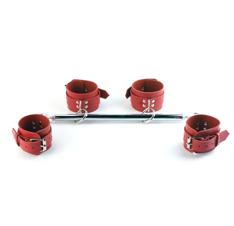 May include: A spreader bar featuring a central chrome-plated metal rod with four red adjustable cuffs attached by silver-toned metal rings. Each cuff is secured with a metal buckle and features multiple adjustment holes for a customized fit.
