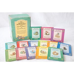 Puede incluir: Una colección de libros de "Peter Rabbit and Friends Library" de Beatrix Potter. El conjunto incluye una caja verde y varios libros pequeños y coloridos con ilustraciones y títulos como "The Tale of Benjamin Bunny" y "The Tale of Mrs. Tittlemouse".
