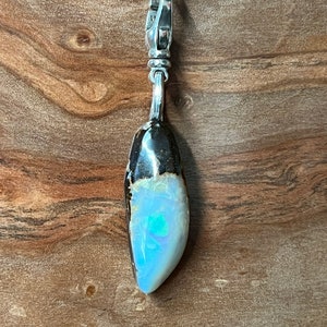 May include: A silver pendant with a black and white opal stone. The opal has a blue and green iridescent sheen.