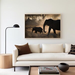May include: A framed photograph of two elephants walking through tall grass in the African savanna. The elephants are silhouetted against a golden sunset. The larger elephant is leading the way, while the smaller elephant follows closely behind.