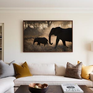 May include: A framed photograph of two elephants walking through a grassy field. The larger elephant is in the foreground, while the smaller elephant is following behind. The elephants are silhouetted against a golden sunset.