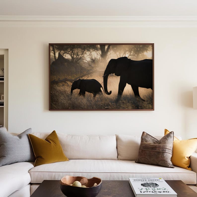 May include: A framed photograph of two elephants walking through a grassy field. The larger elephant is in the foreground, while the smaller elephant is following behind. The elephants are silhouetted against a golden sunset.