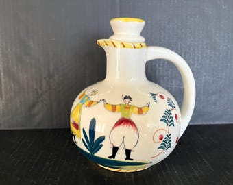 Jarra de cerámica pintada a mano, de estilo folclórico, con tapa, que presenta motivos florales estilizados y figuras de campesinos en colores brillantes; en excelente estado; 19 cm de altura.