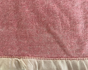 Op de afbeelding: Close-up van een roze geweven stof met een getextureerde uitstraling. De stof heeft een lichtroze tint en een witte, gefranjerde rand langs de onderkant. De weefsel is zichtbaar en creëert een subtiel patroon.