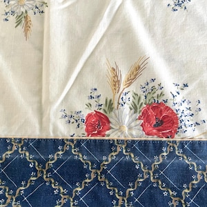 Puede incluir: Tela blanca con un estampado floral de amapolas rojas, margaritas blancas y espigas de trigo. El borde inferior tiene un diseño geométrico azul y dorado. Adecuado para la decoración del hogar.