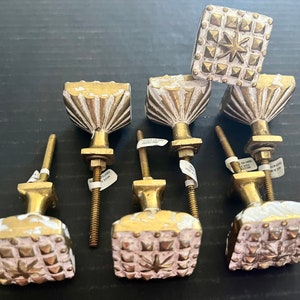 May include: Eight antique-style cabinet knobs with a distressed white finish and gold accents. The knobs have a variety of designs, including a starburst and a fan pattern.
