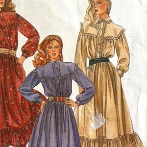 May include: A sewing pattern envelope labeled 8108 featuring illustrations of three long-sleeved dresses with high collars, ruffled yokes, and gathered skirts. The dresses are shown in red floral, solid purple, and solid beige with a dark green belt.