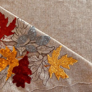 Mantel de 254 cm de largo x 150 cm de ancho, con apliques y detalles calados, con hojas de otoño sobre fondo color camel.