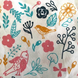 May include: White fabric with a repeating pattern of pink and yellow flowers, teal leaves, and orange birds. The design includes black floral stems and buds, creating a cheerful, nature-inspired aesthetic.