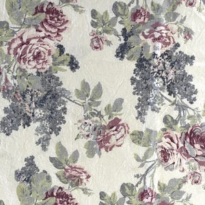 May include: A cream-coloured fabric with a floral pattern featuring pink and grey roses and leaves. The fabric has a textured surface.