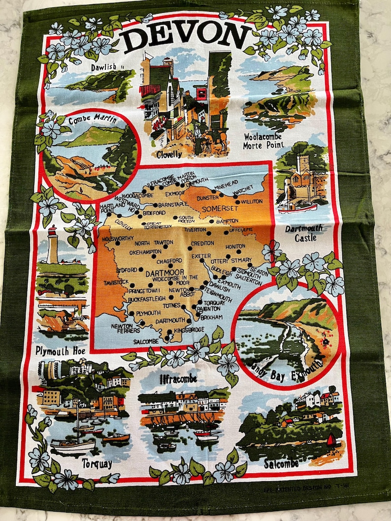 May include: A green tea towel with a map of Devon, England. The map features various towns and cities, including Plymouth, Torquay, and Dartmouth. The tea towel is decorated with floral borders and has a red and white border.