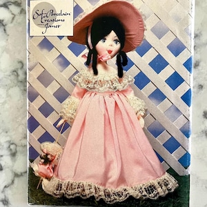 May include: A vintage porcelain doll wearing a pink dress with lace trim, a matching hat, and a small purse. The doll has black hair and is set against a blue and white lattice background. The doll is from Soft Porcelain Creations Janet.