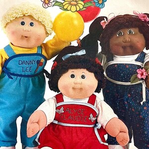 May include: Three dolls with yarn hair and fabric bodies. One doll has blonde hair and blue overalls with the text DANNY LEE. Another has dark hair and a red dress with the text ALYCE CLAUDIE. The third has dark pigtails and a floral blue jumpsuit.
