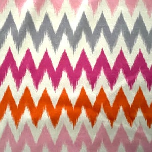 May include: A fabric with a repeating chevron pattern in shades of pink, orange, gray, and white. The zig-zag design creates a bold, textured look, suitable for home decor or fashion applications.