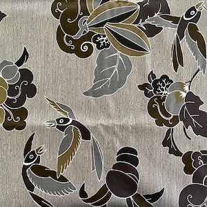 Könnte beinhalten: Ein beigefarbener Stoff mit einem sich wiederholenden Muster aus stilisierten Vögeln und floralen Motiven in Braun-, Schwarz- und Grautönen.
