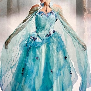 Puede incluir: Un vestido de fantasía azul claro con una falda en capas y mangas transparentes y fluidas. El corpiño está adornado con adornos florales. El vestido tiene un cuello alto y un delicado collar. El diseño general evoca un tema de cuento de hadas o fantasía.