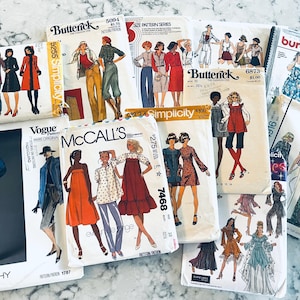 May include: A collection of vintage sewing pattern envelopes featuring illustrations of various clothing designs. Brands include Butterick, Simplicity, Vogue, McCall's, and Burda. The patterns showcase dresses, coats, and other garments, with a variety of styles and colors.