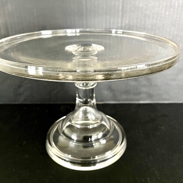 assiette à gâteau en verre pressé vintage sur piédestal en forme de cloche, bord surélevé, pas d'éclats ni de fêlures mais rayures de couteau sur l'assiette ; 7,5 po. de haut x 10,25 po.