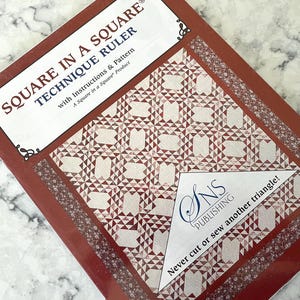 Puede incluir: Un libro rojo y blanco titulado "Square in a Square Technique Ruler" con instrucciones y patrones. La portada presenta un diseño de edredón geométrico en rojo y blanco. El libro es un producto "Square in a Square".