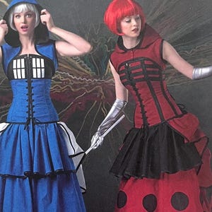 Op de afbeelding: Twee vrouwen in cosplay-kostuums. De ene draagt een blauwe jurk met een zwart-wit lijfje, de andere een rode jurk met zwarte accenten en een zwarte rok met grote zwarte stippen. Beide jurken hebben een korsetachtig ontwerp.