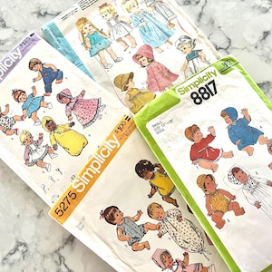Pode incluir: Três moldes de costura Simplicity para bonecas, numerados 7208, 5275 e 8817. Cada envelope de papel apresenta ilustrações coloridas de bonecas vestindo várias roupas, incluindo vestidos, macacões e toucas, com etiquetas de tamanho para bonecas de 33 a 36 cm.