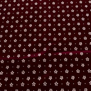 May include: Burgundy fabric with a repeating pattern of small white flowers and dots. The floral design is evenly spaced across the material, creating a consistent and visually appealing texture. Ideal for sewing projects.