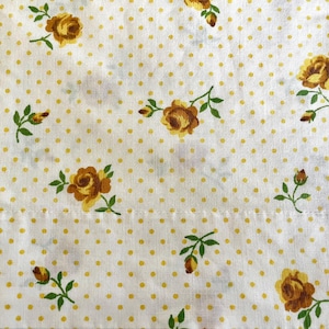 May include: White fabric featuring a pattern of yellow polka dots and yellow roses. The roses have brown centres and green leaves. The fabric is suitable for sewing or craft projects.