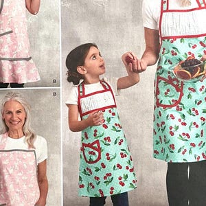 May include: Aprons in various styles and sizes, featuring a pink bunny print and a green cherry print. The aprons have pockets and contrasting trim. One apron is worn by a child, and another by an adult. The aprons are designed for kitchen use.