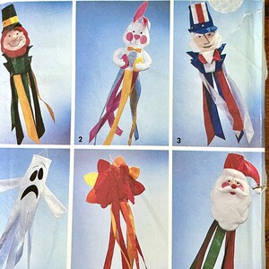 May include: A collection of whimsical windsock decorations featuring various characters. The designs include a leprechaun, a bunny holding an egg, Uncle Sam, a ghost, a flower, and Santa Claus. Each windsock has colorful streamers.