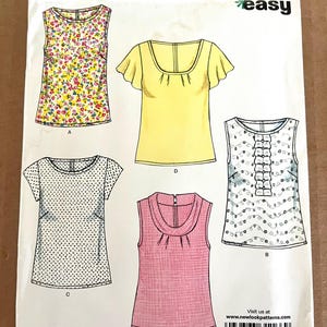 May include: A New Look sewing pattern envelope featuring illustrations of five different tops. The tops include a floral print, a yellow top with ruffled sleeves, a polka dot top, a pink top, and a white top with ruffles.