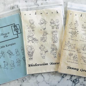 Może przedstawiać: Trzy pakiety ze wzorami do szycia w stylu vintage w plastikowych osłonach. Pakiety są jasnoniebieskie, kremowe i beżowe. Na jasnoniebieskim pakiecie widnieje napis "Tracing the Past Little Kewpies". Na kremowym pakiecie widnieje napis "redwork Wiederseim Nurse". Na beżowym pakiecie widnieje napis "redwork Penny Goose".