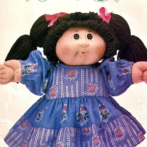 May include: A soft-sculpture doll with dark brown yarn hair styled in two pigtails with pink bows. The doll has a round face with rosy cheeks and wears a blue long-sleeved dress featuring a pattern of vertical white stripes and small pink roses.